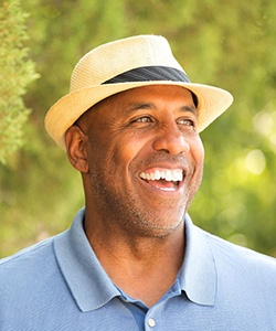 Man in fedora and blue polo smiling with dental bridges in Assonet