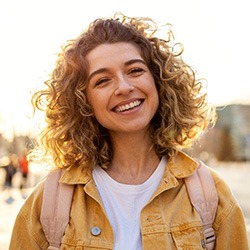 a smiling person standing outside wearing a backpack and a yellow jacket