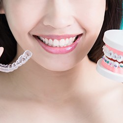 A young female holding a ClearCorrect aligner in one hand and a mouth mold with traditional braces in the other hand