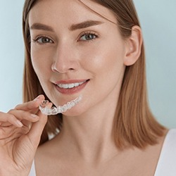 A woman wearing a white tank top and preparing to insert her ClearCorrect aligner after cleaning it