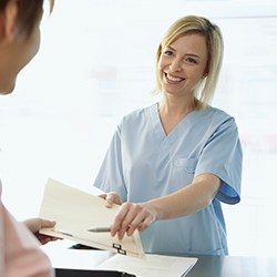 Smiling team member giving patient paperwork explaining the cost of treating dental emergencies