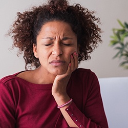 Woman rubbing her jaw in pain while sitting on couch