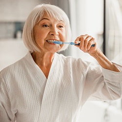 Senior woman wearing a bathrobe and brushing her teeth
