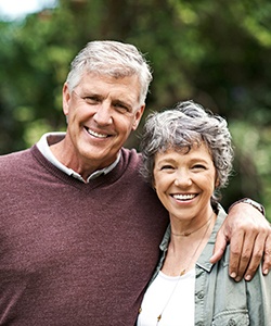 Happy couple with dental implants in Assonet standing outside