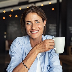 Smiling woman with dental implant replacement teeth holding a white coffee mug