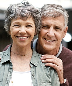 Older man and woman smiling after replacing missing teeth