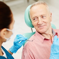 Smiling older man in dental chair discussing tooth replacement options