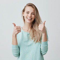 Woman smiling with thumbs up after porcelain veneer treatment