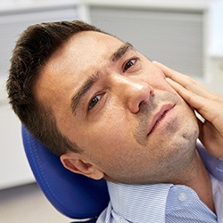 Man in dental chair holding cheek before restorative dentistry