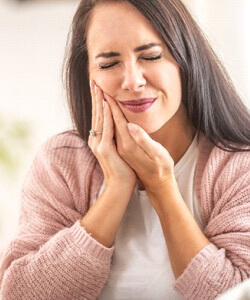 a woman holding her cheek due to failed dnetal implant