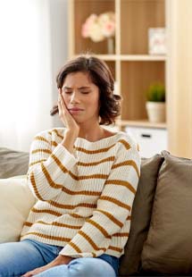 Woman in dental chair holding cheek before restorative dentistry