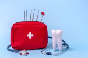 Model tooth next to red emergency bag with dental and medical equipment on a light blue background